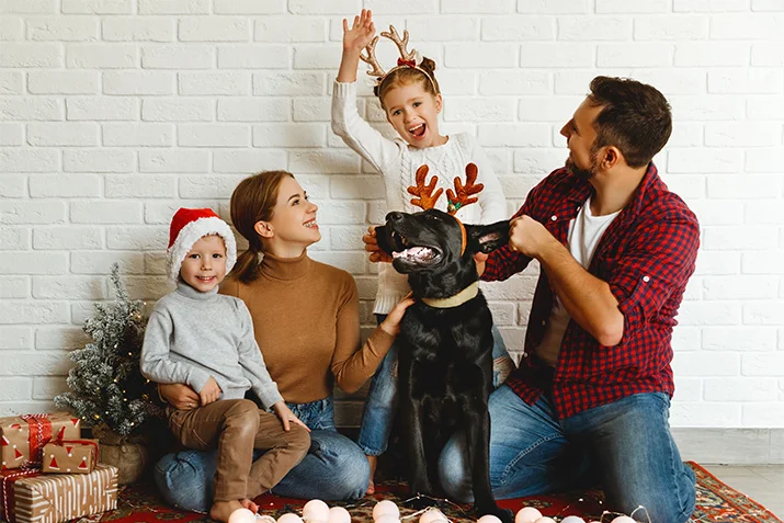 Family celebrating the holidays with a black dog wearing reindeer antlers